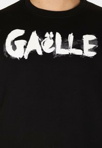 T-shirt in cotone nero con grande scritta bianca in stile pennellata che recita "GAËLLE" sul petto, con dettagli testurizzati.