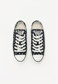 Fekete vászon sportcipők fehér pöttyökkel, fehér fűzőkkel és gumitalppal. A nyelvén a "Converse All Star" márkajelzés található.