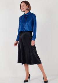 Blue satin blouse with a tied collar, paired with a flowing black satin midi skirt. Model wears black high heels and large hoop earrings.