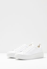Hvite lær sneakers med rund tå, snøring foran og teksturert gummisåle. Har en løkke på hælen for enkel påføring.