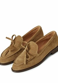 Béžové semišové mokasíny mají zaoblenou špičku, přední mašličku a nízkou hnědou koženou podrážku. Měkká textura a klasický design.