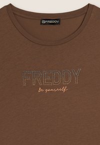 T-shirt marrone a maniche corte con la scritta "FREDDY" in strass, accompagnata dalla scritta in corsivo "be yourself" sotto. Tessuto morbido e scollatura rotonda.