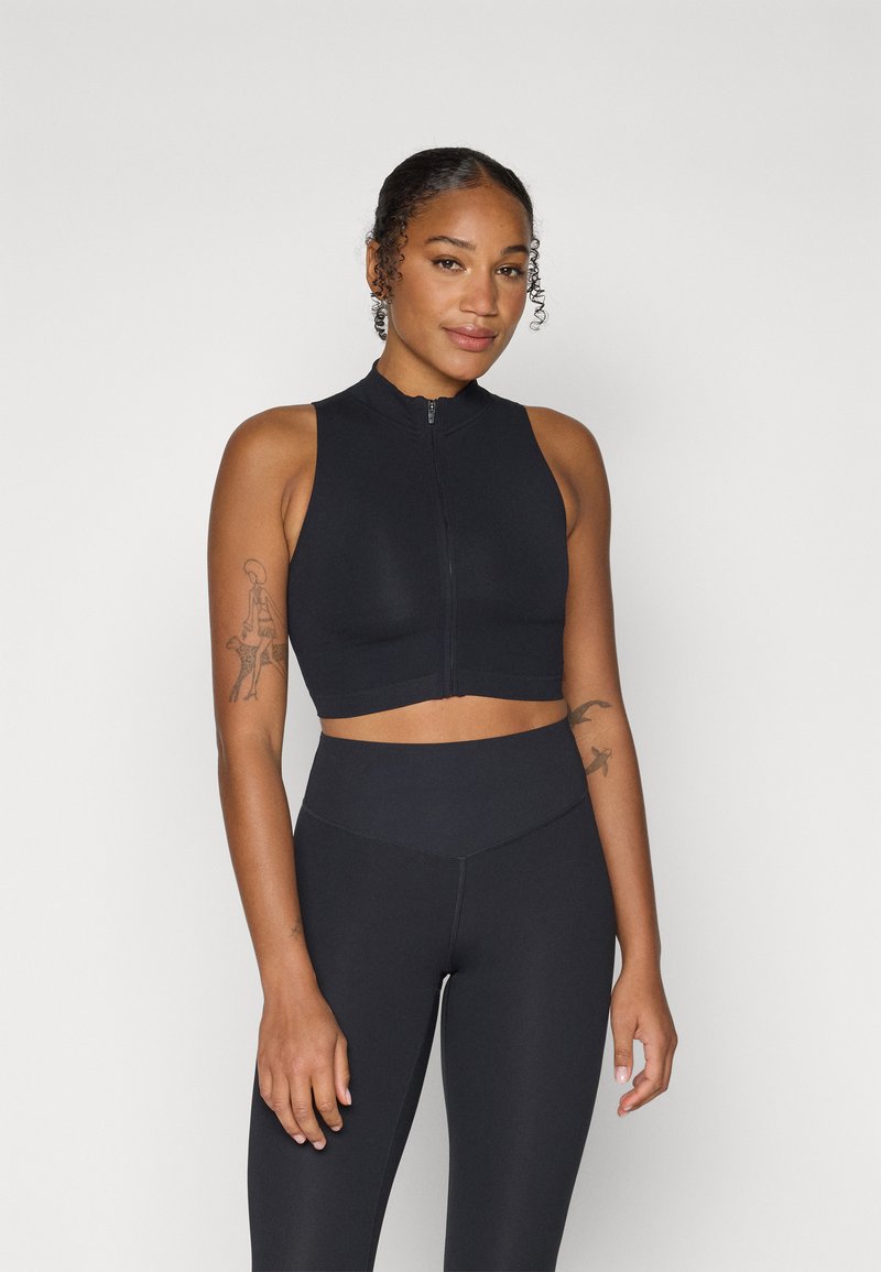 Crop top sportivo nero con colletto alto e zip frontale, realizzato in tessuto liscio e elastico. Abbinato a leggings a vita alta coordinati.