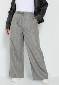 Grårandiga vida byxor med elastisk midja och dragsko. Matchas med en vit topp och en svart läderjacka.