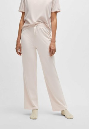 Light pink, loose-fitting pants made of soft fabric with an elastic waistband and drawstring. Paired with a matching light shirt and beige socks.