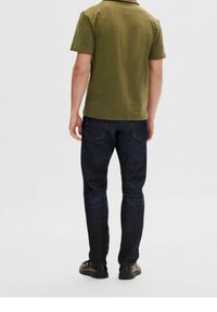 Polo shirt vert olive à manches courtes, associé à un jean en denim bleu foncé. Le jean a une coupe slim et des poches arri ère visibles.