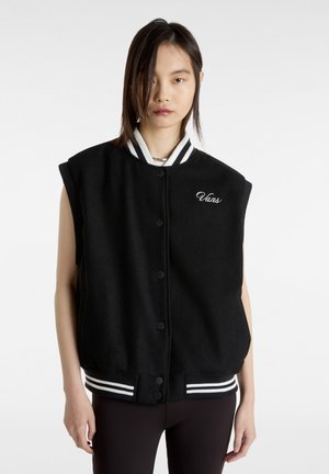 Svart ärmlös varsity-jacka med en ull-liknande textur, vit randig ribbad krage och fåll, med knappstängning och broderad logotyp.