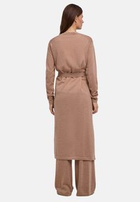 Bruin tweedelig geheel met een lang katoenen vest met riem en broek met brede pijpen, gemaakt van een zachte gebreide stof. Simpel, minimalistisch ontwerp.