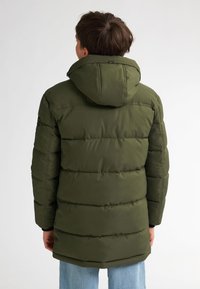 Olivgrüne Steppjacke mit abnehmbarem Kapuzen, horizontaler Steppung und Seitentaschen, getragen über hellblauen Jeans.