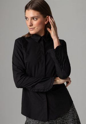 Schwarzes Langarmshirt mit kragenförmigem Ausschnitt und Rüschensaum, aus glattem Stoff gefertigt. Die Passform ist tailliert und hat einen abgerundeten Saum.
