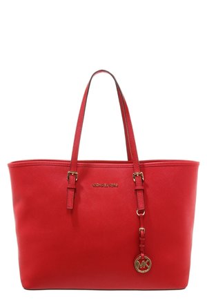Sac fourre-tout en cuir rouge avec deux bretelles, logo Michael Kors doré au centre, et un pendentif rond doré MK suspendu à une des lanières.