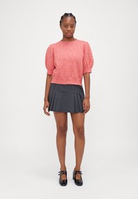 Růžový texturovaný svetr s krátkými nadýchanými rukávy, zkombinovaný s šedou skládací sukní. Černé lakované boty doplňují celý outfit.