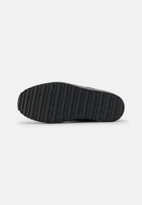 Suela de zapato de goma negra con estrías horizontales y marca en relieve. Superficie texturizada que proporciona agarre y durabilidad. Tacón redondeado y liso.