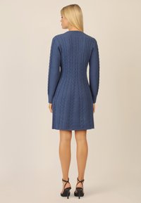 Abito in maglia blu con motivo a treccia, maniche lunghe e scollo rotondo, abbinato a sandali neri con cinturini e tacco alto.
