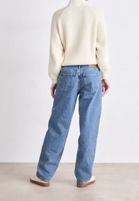 Krämbroderad polokrage tröja som är kombinerad med ljusblå, löst sittande denimjeans med hög midja och fyra fickor. Naturlig texturerad yta.