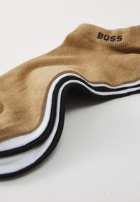 Braune Baumwollsocken mit schwarz-weißen Streifenakzenten, ausgestattet mit einem gerippten Bündchen und dem "BOSS"-Logo in Schwarz auf der Oberseite.