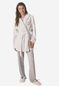 Hvid, blød badekåbe med hætte og bindebånd i taljen, prydet med et subtilt kaninmønster. Sammen med grå bukser med leopardmønster og dyreformede slippers.
