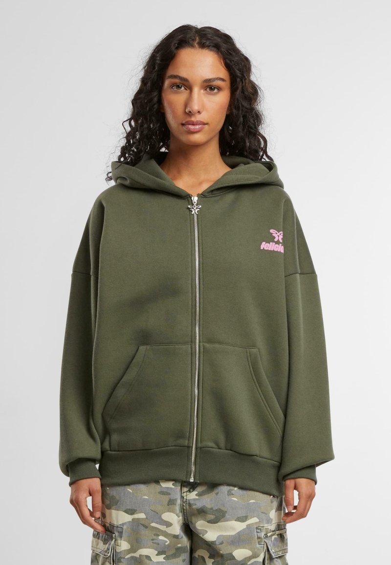 Olivgrön zip-up hoodie i mjukt material. Har en luva, rosa logotyp på bröstet och två framfickor. Lössittande passform med ribbade ärmslut.