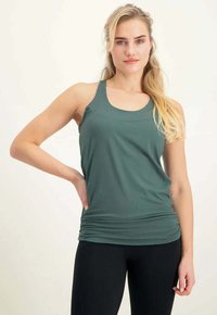 Dunkelgrünes ärmelloses Tanktop mit rundem Ausschnitt, aus weichem Stoff gefertigt. Verfügt über eine geraffte Detail am Bund, kombiniert mit schwarzen Leggings.