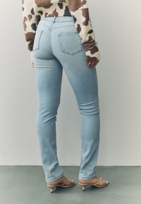 Svijetloplave uske traperice s visokom strukom srednje visine, s dva stražnja džepa i glatkom teksturom. Uparene s bež sandalama otvorenih prstiju.