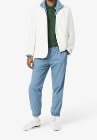 Biała marynarka na zielonym polo i niebieskie spodnie dresowe. Materiał jest gładki. Cechy obejmują kontrastujący kołnierz, elastyczne mankiety oraz sneakersy.