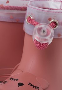 Stivale di gomma rosa con finitura liscia, un piccolo design di faccia d'orso sulla punta e un accento intrecciato con un bottone trasparente.