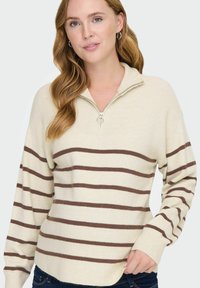 Sudadera cremosa con cremallera, con rayas horizontales marrones, textura acanalada, mangas largas y dobladillo redondeado.