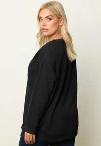 Svart oversized sweatshirt med rund halsringning, ribbade ärmslut och avslappnad passform. Tillverkad av mjukt material, har en slät yta och enkelhet.