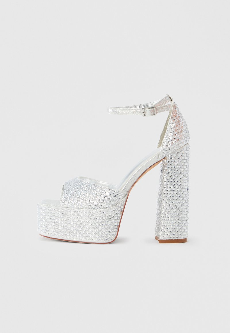 Srebrni platformni čevlji z okraski iz kristalčkov in odprtim prednjim delom. Imajo trak okoli gležnja in teksturiran blok peto.
