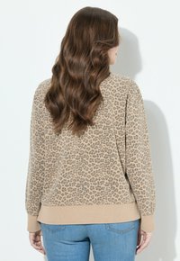 Beżowa bluza z wzorem w cętki lamparta, z prążkowanymi ściągaczami na mankietach i dole, o luźnym kroju i miękkiej fakturze.