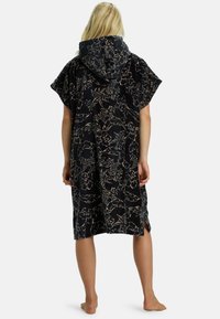 Cubierta de playa con capucha en suave tela negra que presenta un patrón floral en beige. Mangas amplias y aberturas laterales para mayor facilidad de movimiento.