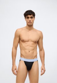 Svart thong undertøy med en lysegrå Calvin Klein-logo på midjebåndet. Stoffet ser glatt og elastisk ut, og følger kroppens konturer.