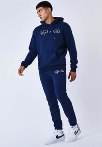 Sudadera con capucha azul marino con texto blanco "Project x Paris", bolsillo frontal y pantalones a juego con logo. Presenta una textura suave y puños acanalados.