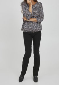 Blouse à imprimé floral avec des manches trois-quarts en marine, associée à un pantalon noir à jambe droite. Tissu texturé et détails de conception simples.