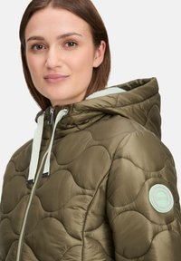 Olijfgroen gewatteerde pufferjack met capuchon, met een mintgroene logo-opdruk, zilveren rits en contrasterende trekkoorden. Gladde textuur.