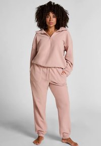 Lichtroze fleece loungewear set met een hoogsluitende top met ritssluiting en taps toelopende broek met elastische tailleband en zakken.