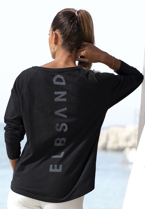 Schwarzes Langarm-T-Shirt mit grauem "ELBSAND" Druck auf dem Rücken, locker geschnitten und aus weichem Material. Empfohlene Kombination mit weißen Hosen.