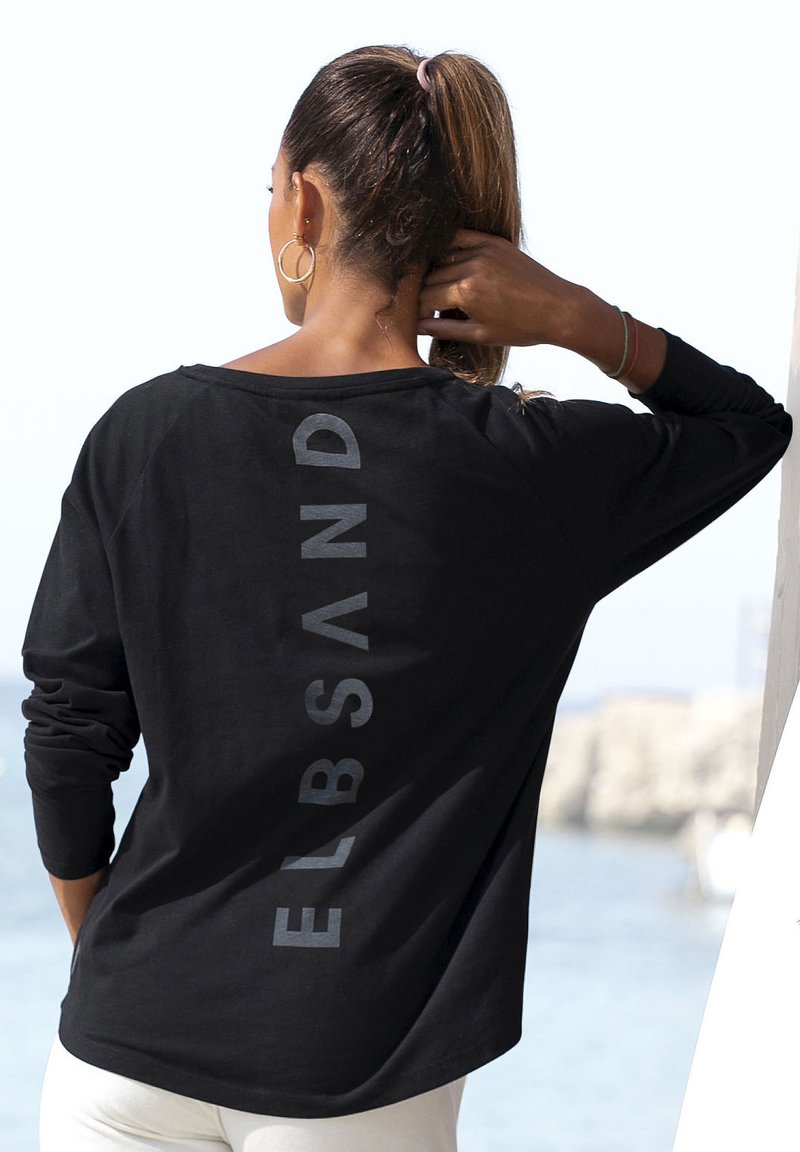 Schwarzes Langarm-T-Shirt mit grauem "ELBSAND" Druck auf dem Rücken, locker geschnitten und aus weichem Material. Empfohlene Kombination mit weißen Hosen.