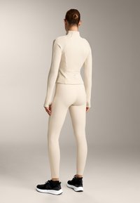 Form-fitting activewear set in light beige, featuring a textured long-sleeve top and matching leggings, paired with black athletic shoes.