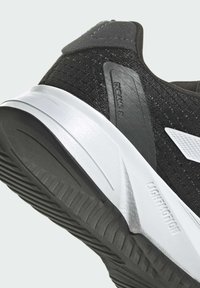 Scarpa sportiva nera con tomaia in rete texturizzata, intersuola bianca e suola esterna in gomma nera. Presenta un logo sul lato e un design scolpito.