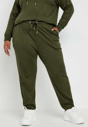 Olivgrüne gerippte Jogginghosen mit Kordelzugbund, seitlichen Taschen, schmal zulaufenden Beinen und getragen mit weißen Turnschuhen. Strukturiertes Stoffdetail sichtbar.