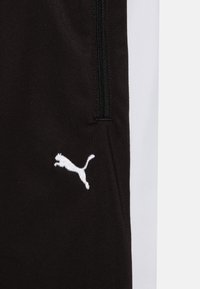 Schwarze Sporthosen mit einem weißen Seitenstreifen, ausgestattet mit einer Reißverschlusstasche und einem weißen gestickten Logo eines springenden Pumas auf dem Stoff.