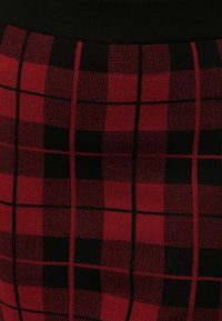 Jupe à carreaux rouge et noir avec une taille élastique noire, un tissu texturé et des motifs à grille horizontaux et verticaux.