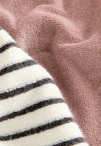 Två handdukar: en i en enda dammig rosa färg, den andra vit med svarta ränder. Båda har en texturerad, mjuk tygkvalitet med en plyschig look.