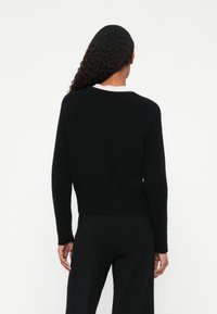 Sweater preto de mangas longas com decote redondo e barra canelada, feito de um tecido de malha texturizada. A vista traseira mostra um corte solto.