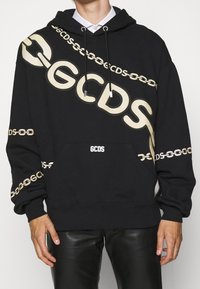 Felpa con cappuccio nera caratterizzata da un audace logo "GCDS" beige e un motivo a catena. Realizzata in tessuto morbido con tasca frontale e cappuccio con cordini.