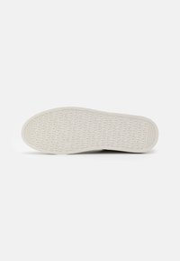 White rubber shoe sole with an embossed pattern of repeated text. The sole features a textured surface for grip and stability.
