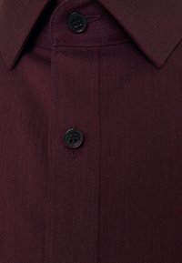 Burgundská košile s dlouhým rukávem, vyrobená z tkaniny s jemným herringbone vzorem, s výrazným límcem a dvěma černými knoflíky na předním zapínání.