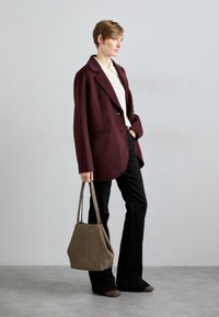 Bordeaux blazer met een gekleed kraag en twee knopen, gecombineerd met zwarte flared pants. Een bruine suède tote bag en gestructureerde schoenen maken de look compleet.