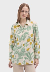Camicia a maniche lunghe realizzata in tessuto leggero, con uno sfondo crema e motivi di foglie verdi e ravanelli gialli, dotata di abbottonatura frontale e colletto.